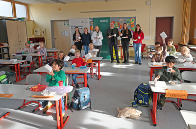Bild vergr��ern: Erstkl�sslerinnen und Erstkl�ssler an der Weinbergschule bekamen das �Gesunde Pausenbrot�. Im Bild hinten (von links): Thea G�tz, Direktorin der AOK in Mittelfranken, Lehrerin Friederun Wirth, Schulleiterin Alrun Schwarz, Oberb�rgermeister Thomas Deffner, Aline L�ffler, Klimaschutzbeauftragte der Stadt Ansbach, und Theresa Deibl.